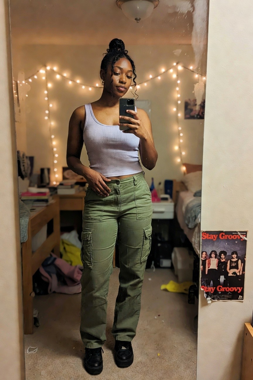 Black woman in light purple ribbed tank top and olive green cargo pants posing for a mirror selfie indoors
