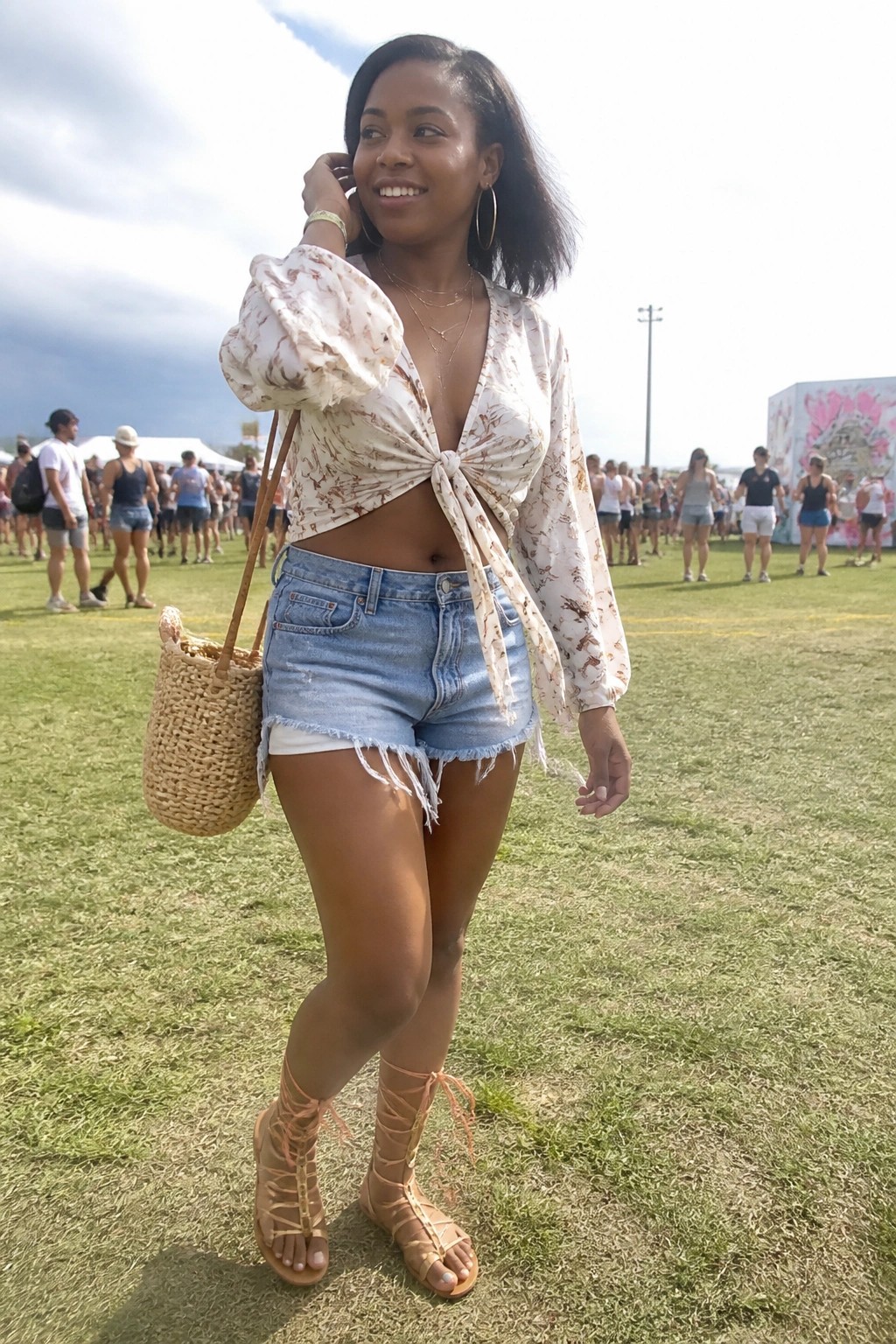 Woman in floral crop top and frayed denim shorts with woven bag at festival