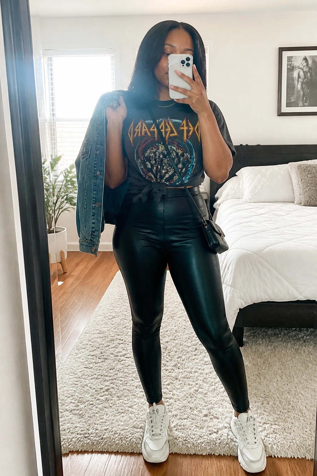 Woman in Def Leppard tee and black leggings holding denim jacket in bedroom mirror selfie