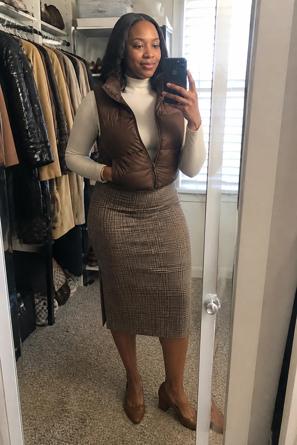 Woman in brown puffer vest and plaid skirt taking closet mirror selfie