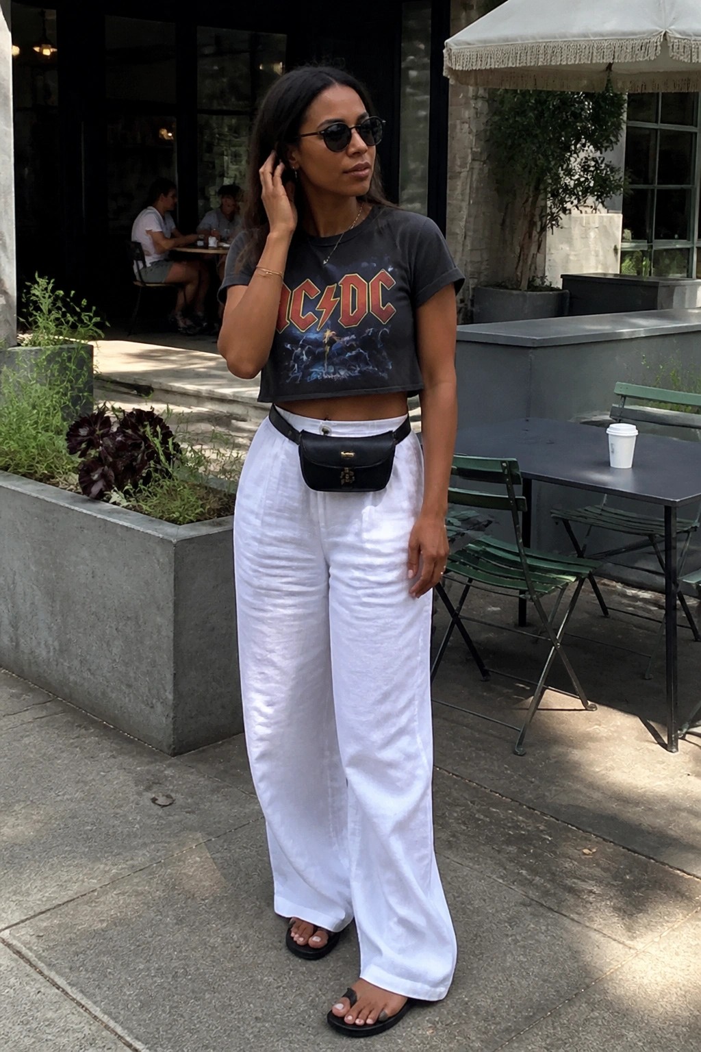 Woman in black AC/DC crop top and white wide-leg pants with black belt bag outdoors