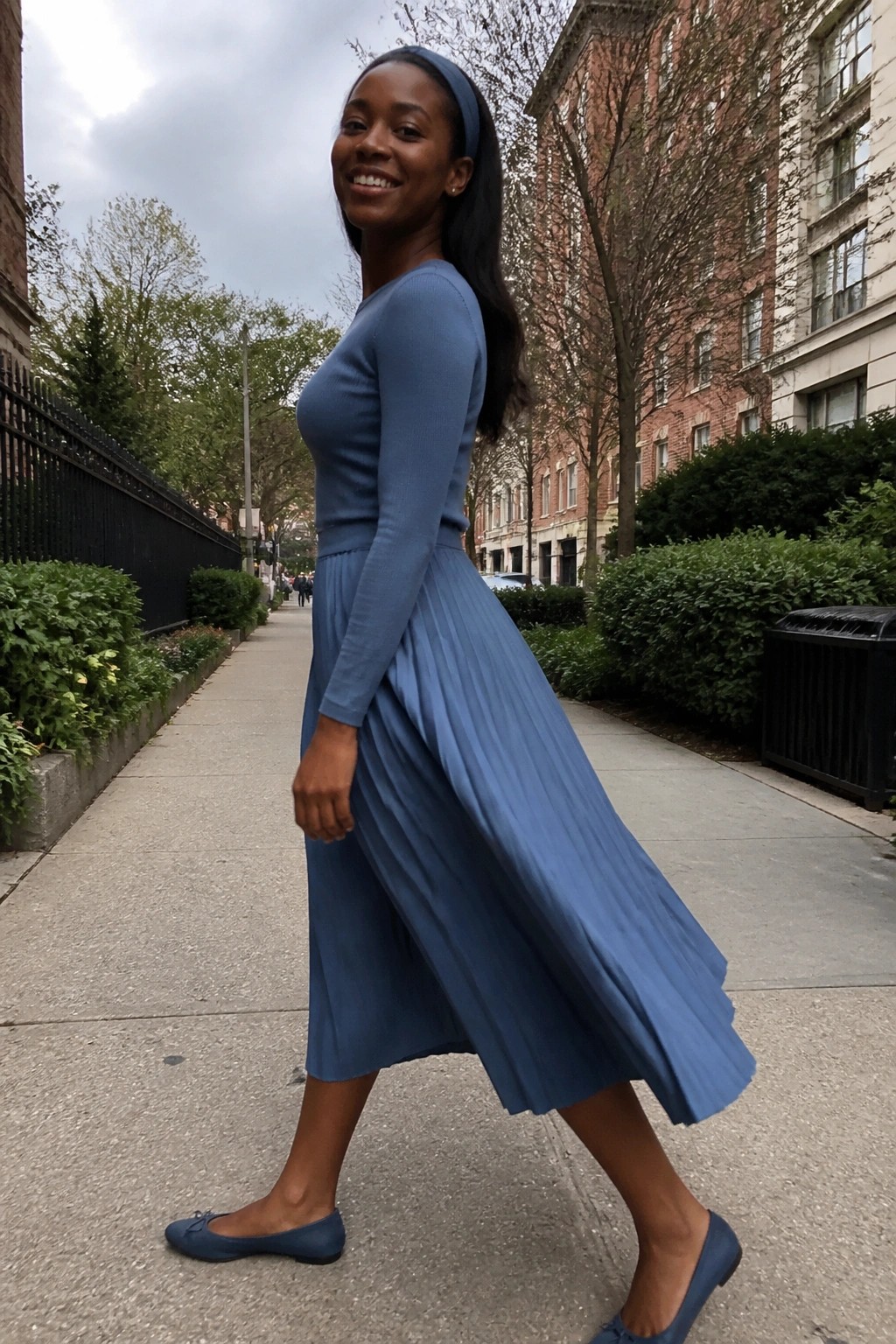 Smiling woman in blue pleated midi skirt and top on city sidewalk