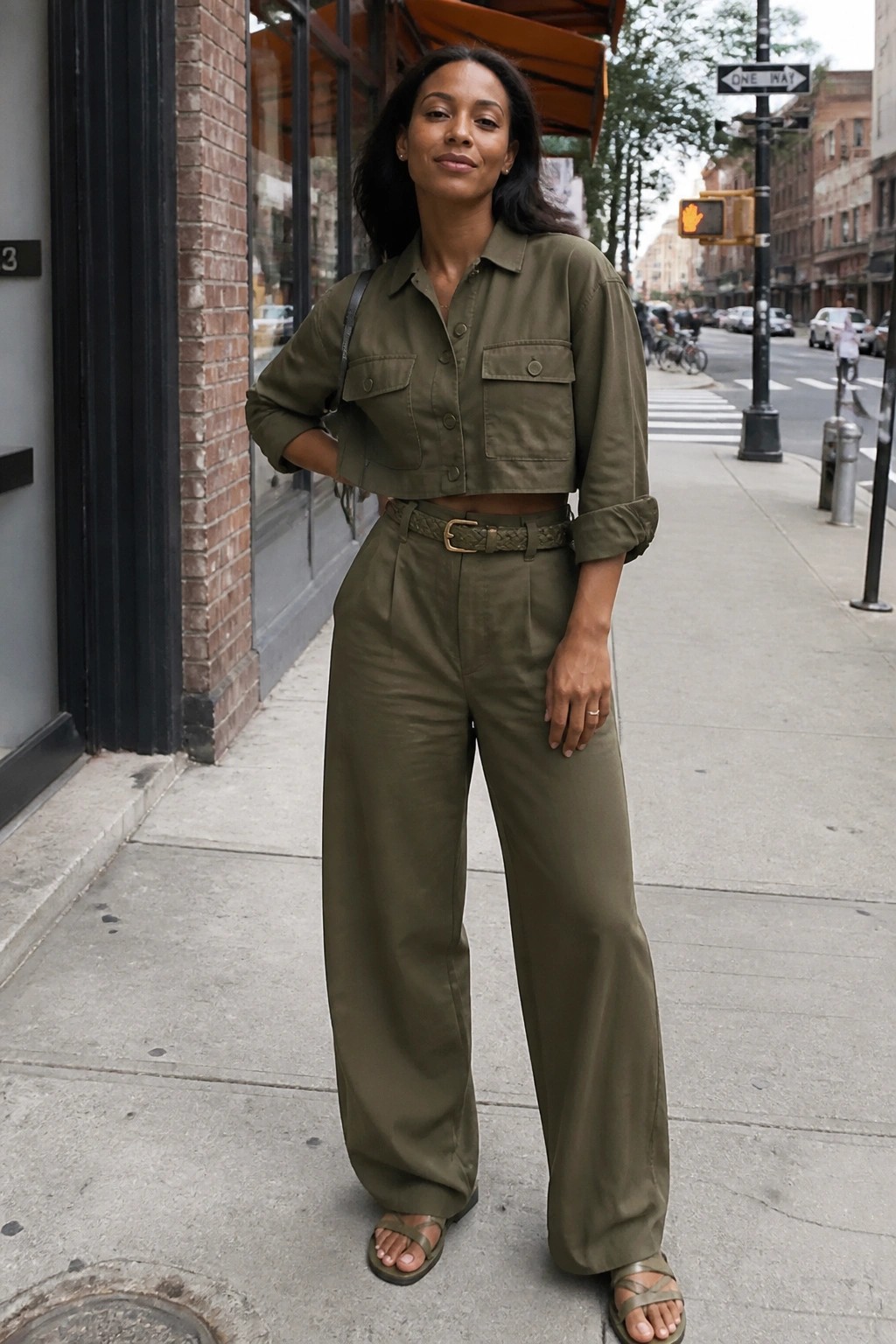 Woman in olive green cropped utility shirt and wide-leg pants on sidewalk.