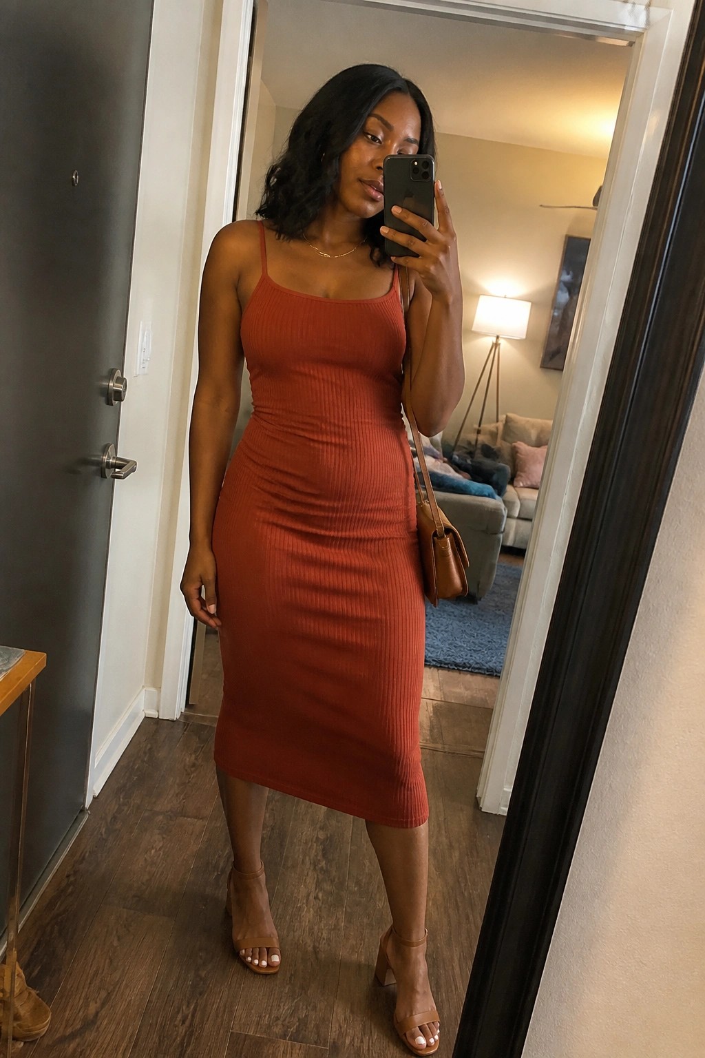 Woman in rust ribbed midi dress taking mirror selfie in apartment