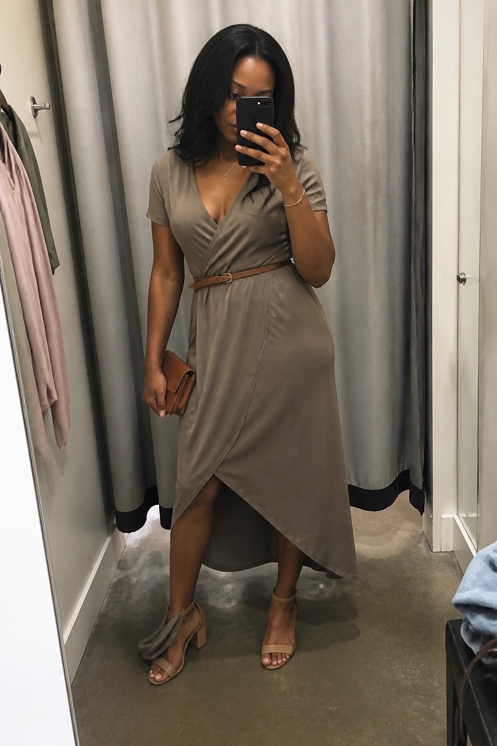 Dark-haired woman in taupe wrap dress takes mirror selfie in fitting room