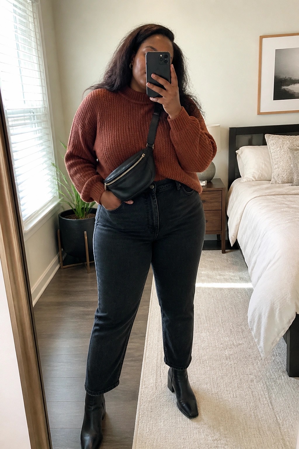 Woman in rust sweater and black jeans taking bedroom mirror selfie with fanny pack