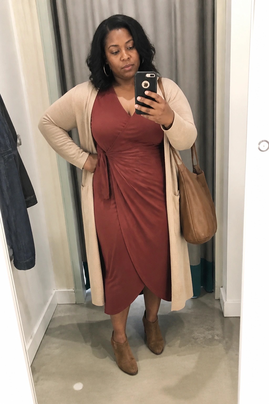 Woman in rust wrap dress and beige cardigan taking mirror selfie in fitting room
