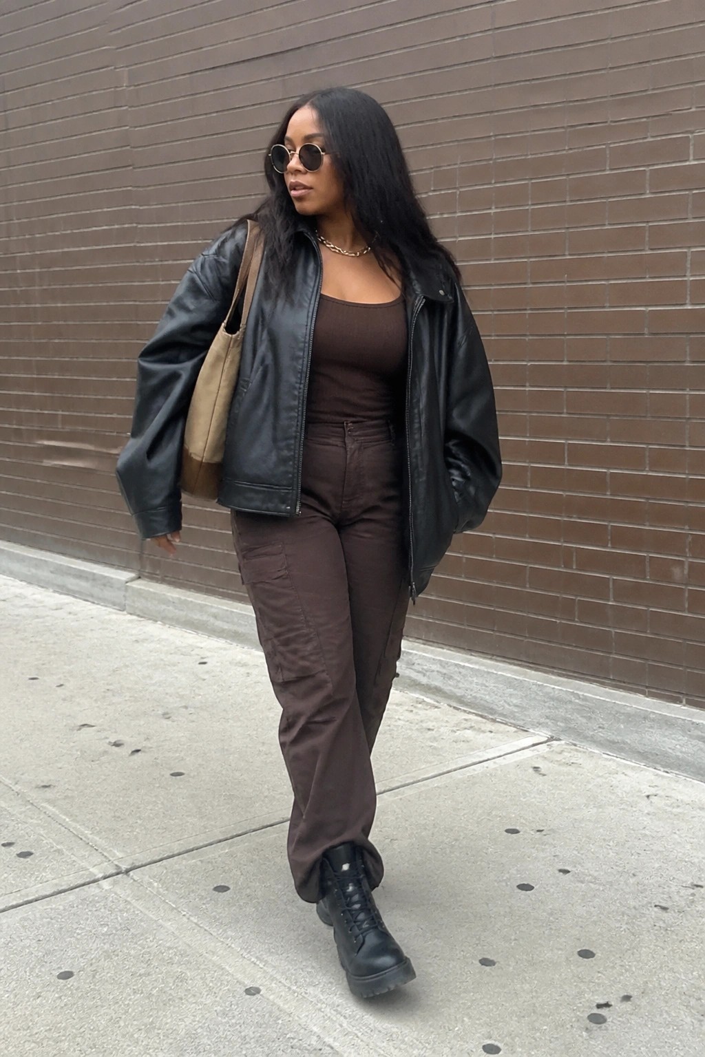 Woman in black leather jacket and brown cargo pants walking on sidewalk