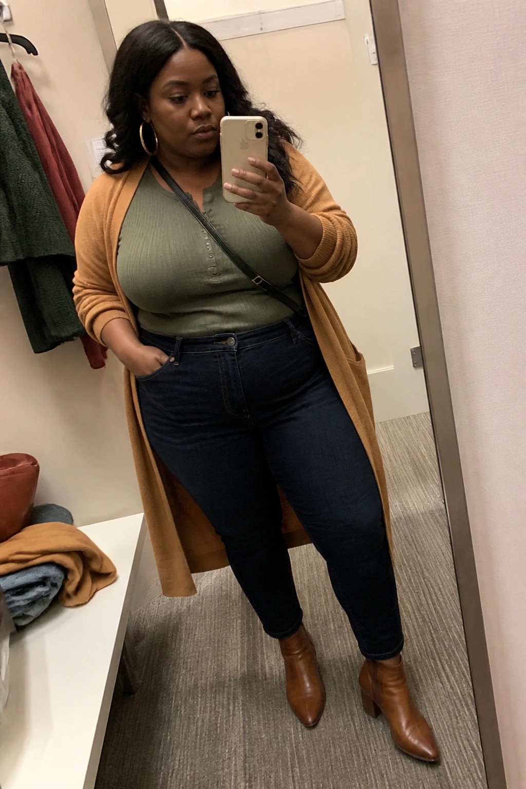 Plus-size woman in mustard cardigan and green top taking mirror selfie in fitting room