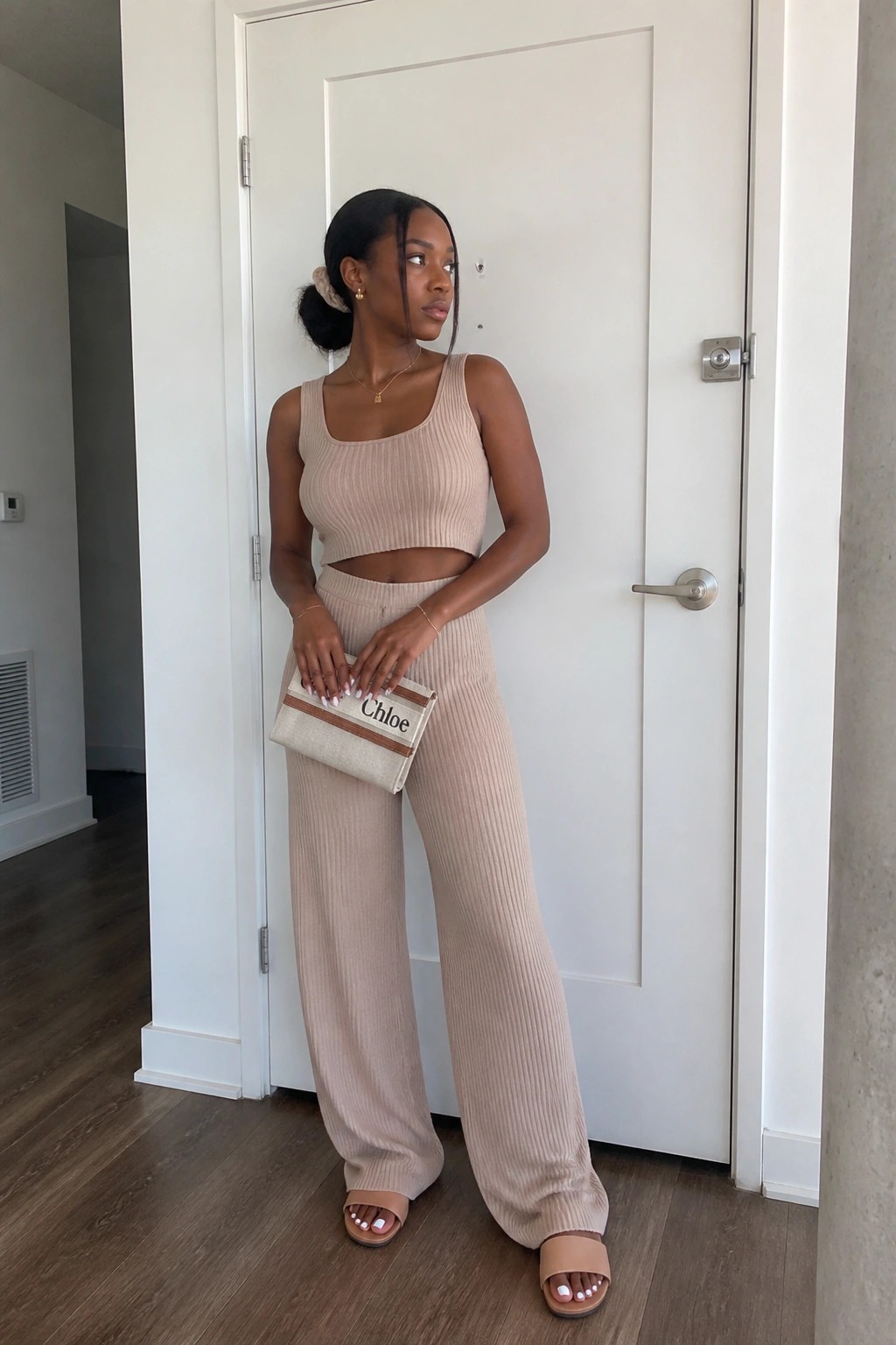 Woman in beige ribbed knit crop top and wide pants holding Chloe clutch.
