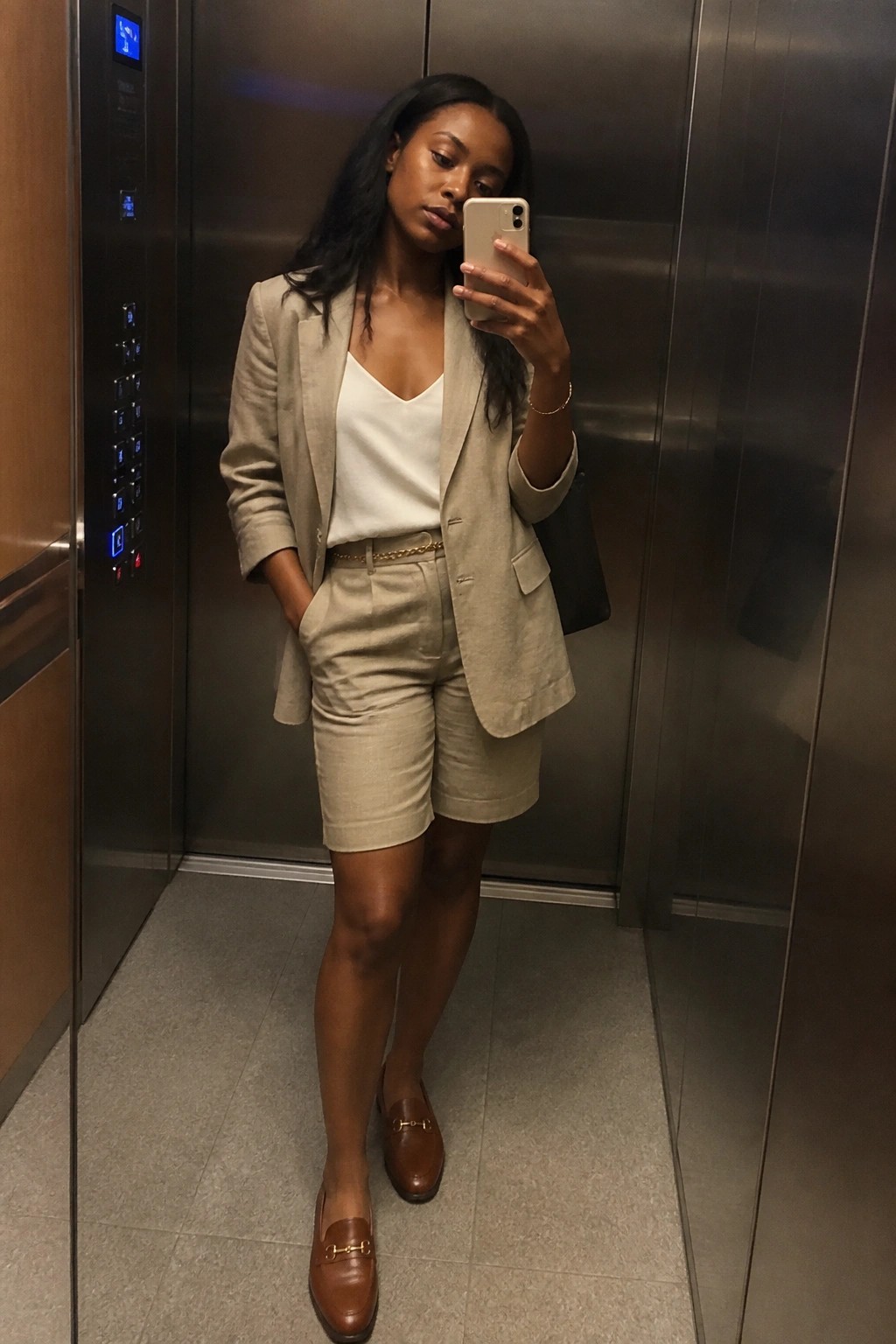 Woman in beige blazer and shorts taking selfie in elevator