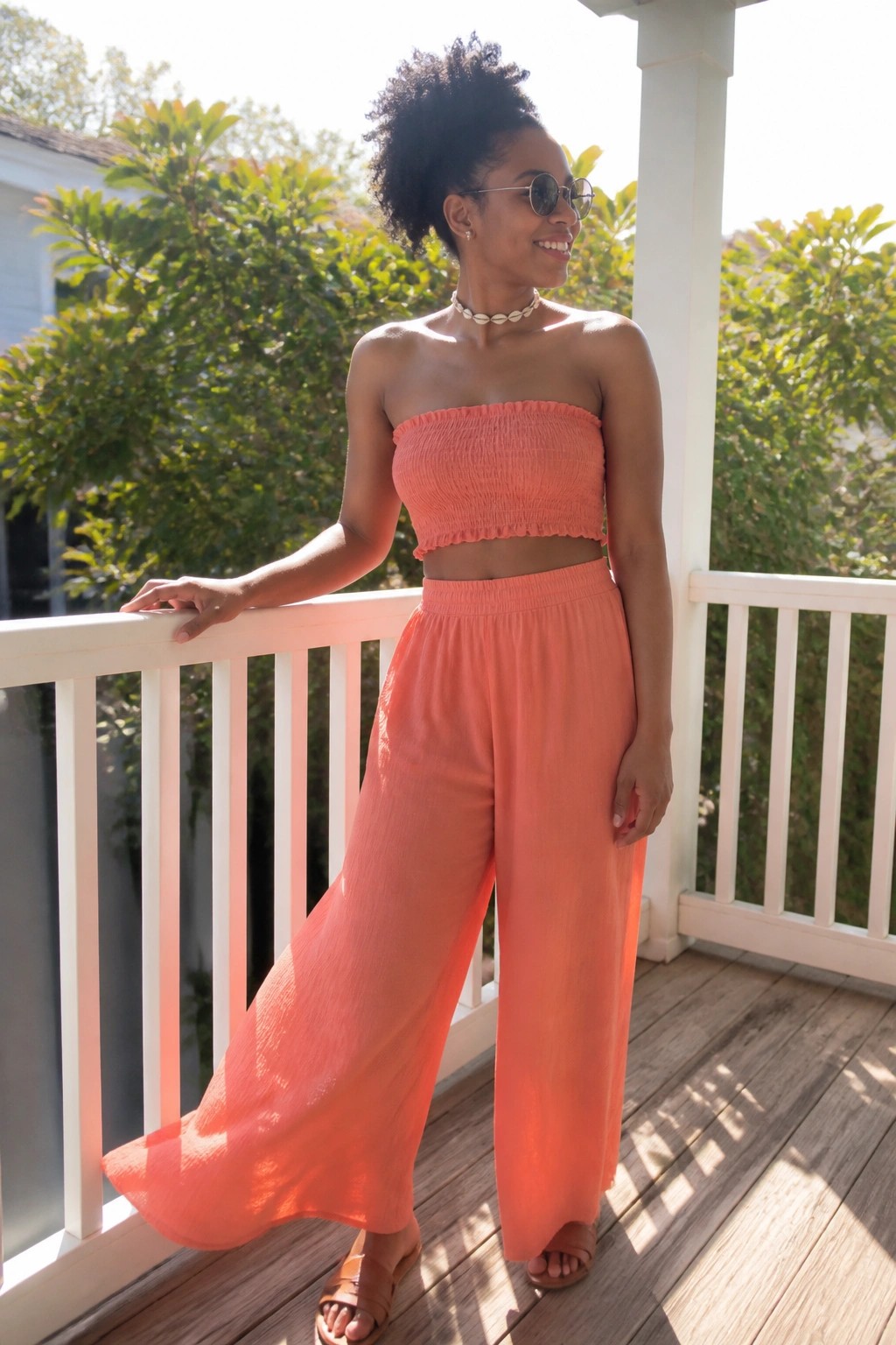 Woman in coral smocked crop top and wide-leg pants on sunny porch