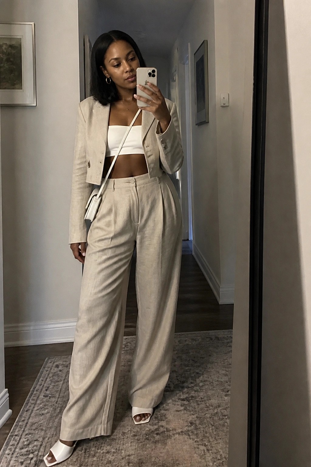 Woman in beige cropped blazer and wide-leg pants taking mirror selfie in hallway