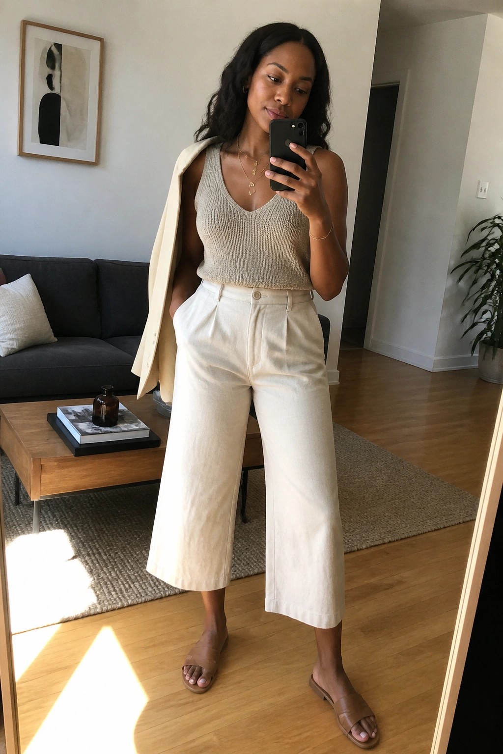 Woman in beige knit top and white wide-leg pants with draped blazer taking mirror selfie