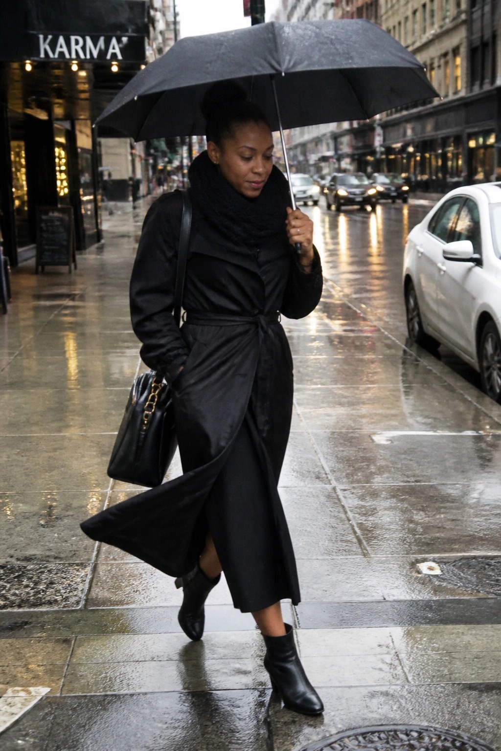 Woman in black coat holding umbrella while walking on rainy city street