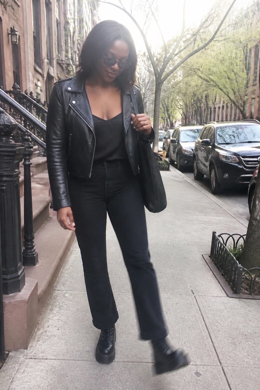 Woman in black leather jacket and jeans walking on city sidewalk