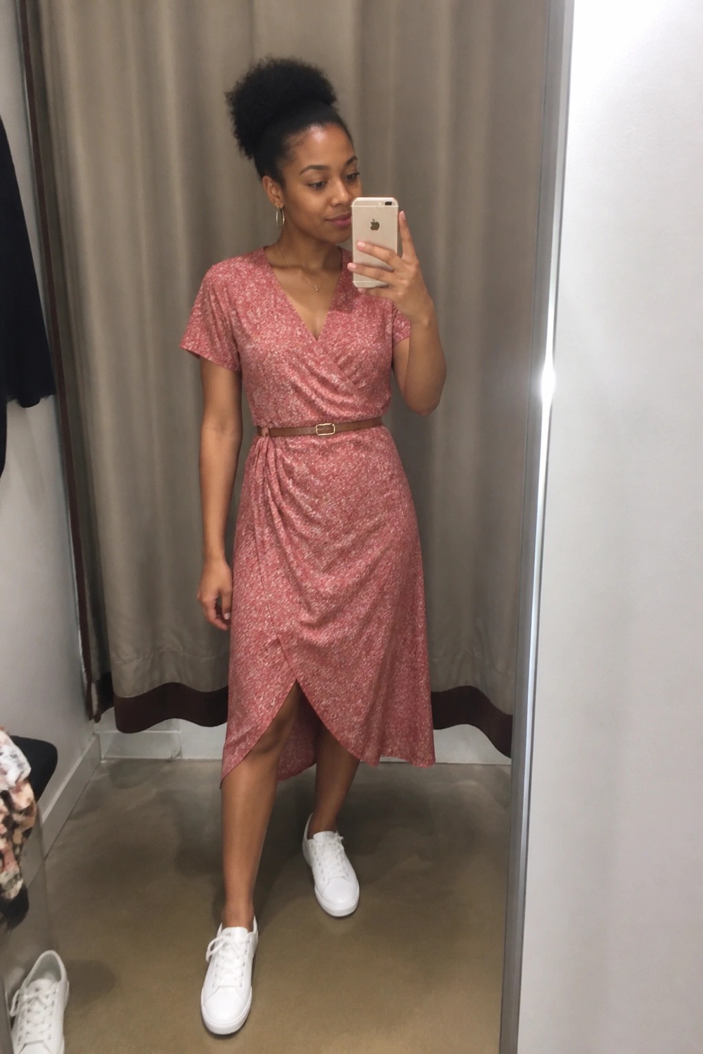 Woman in pink floral wrap dress taking mirror selfie in white sneakers