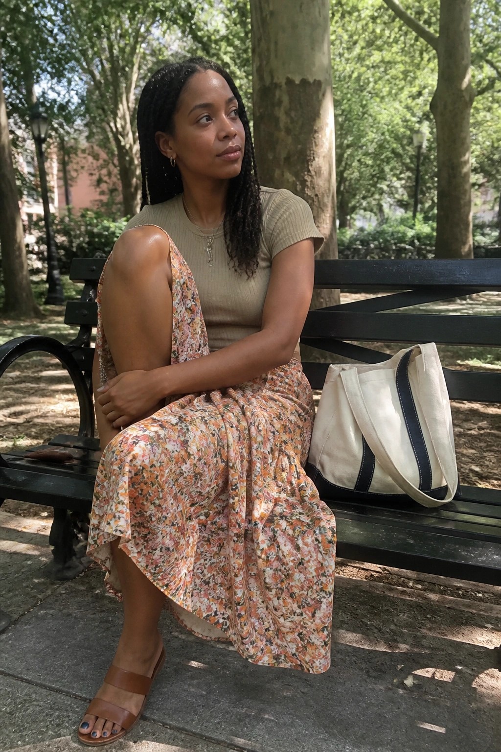 Woman in floral skirt and beige top on park bench with tote bag