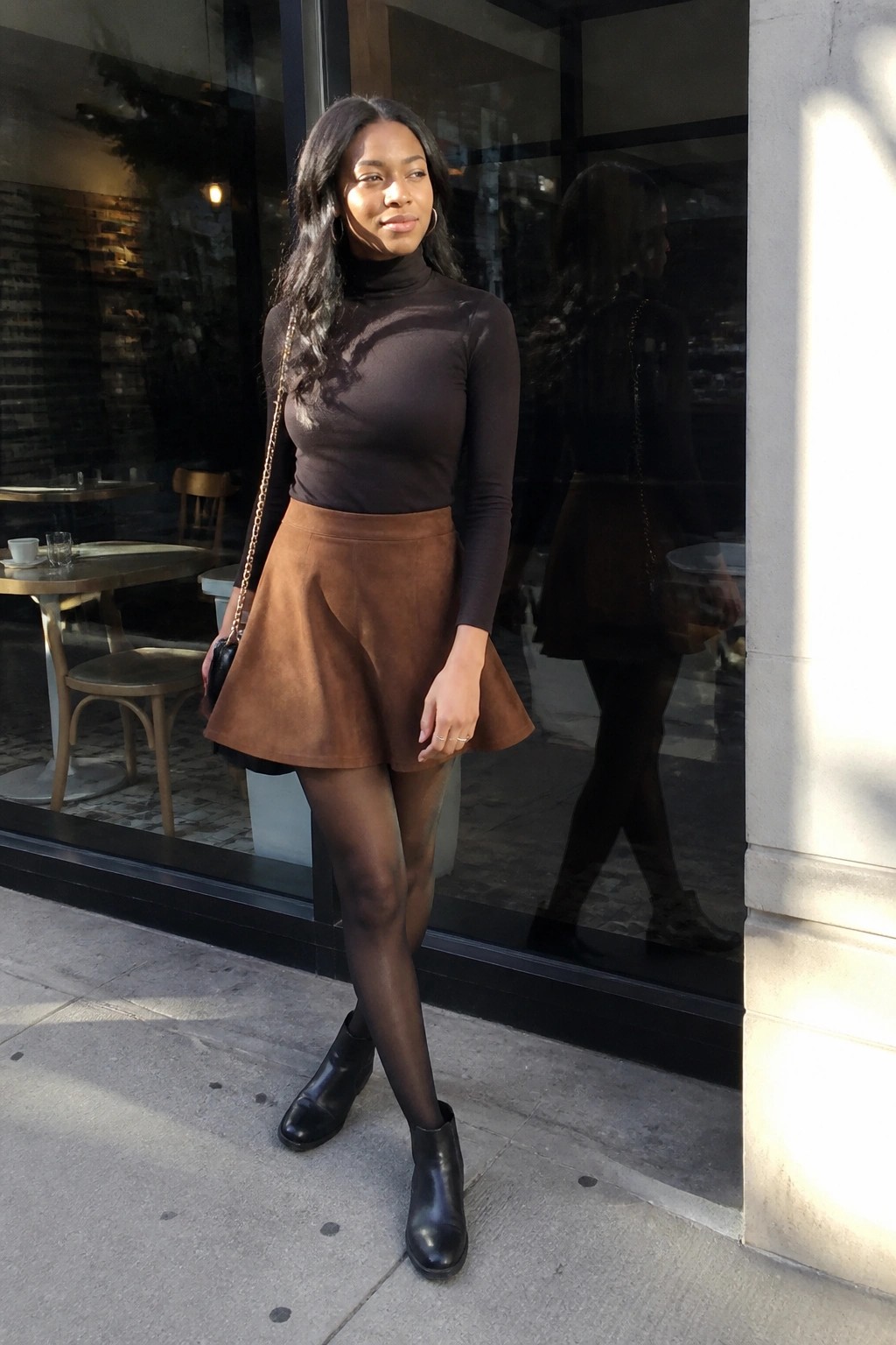 Woman in brown turtleneck and suede skirt outside cafe window with reflection.