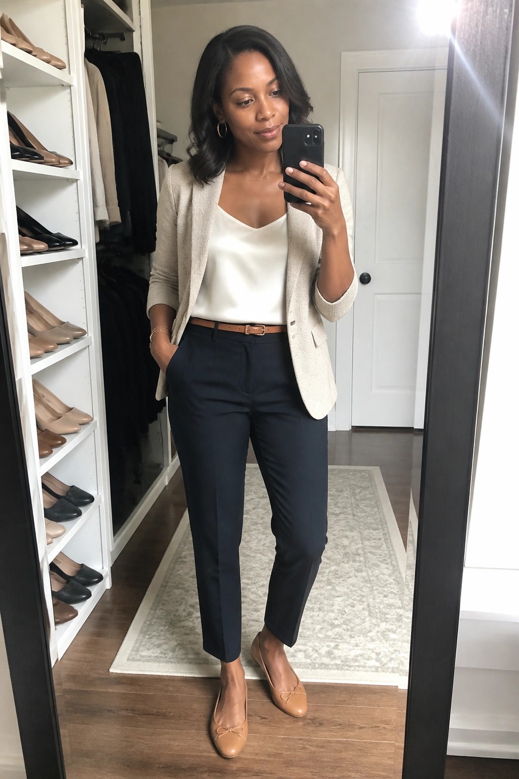 Woman in beige blazer and navy pants taking mirror selfie in closet