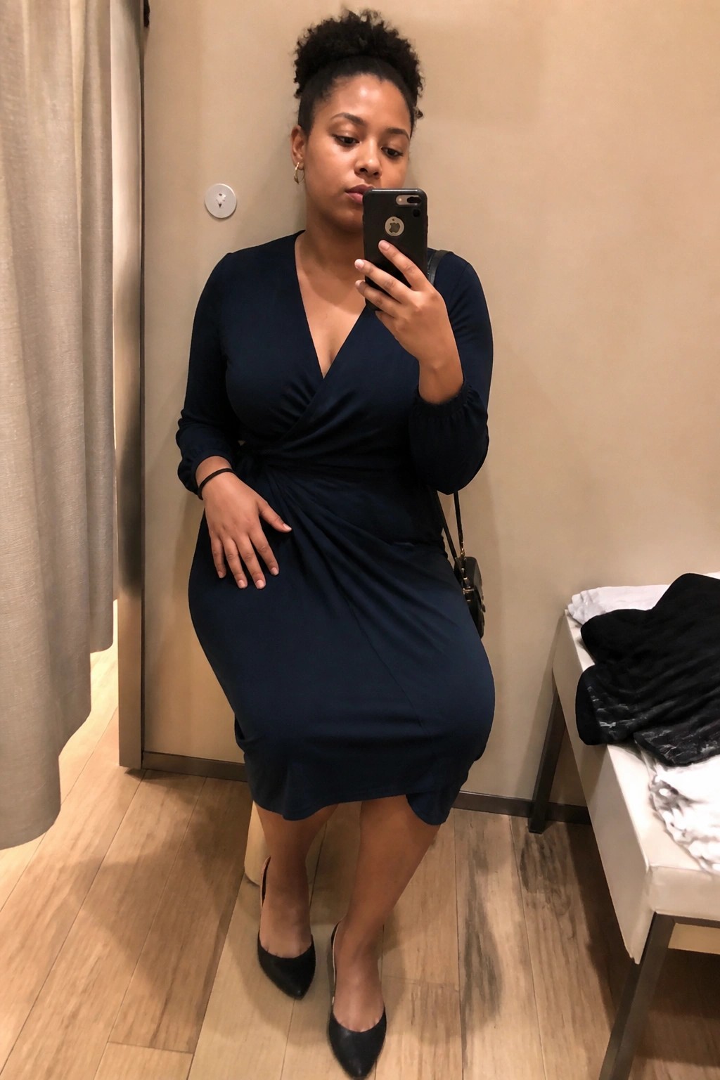 Woman in navy blue wrap dress taking mirror selfie in fitting room