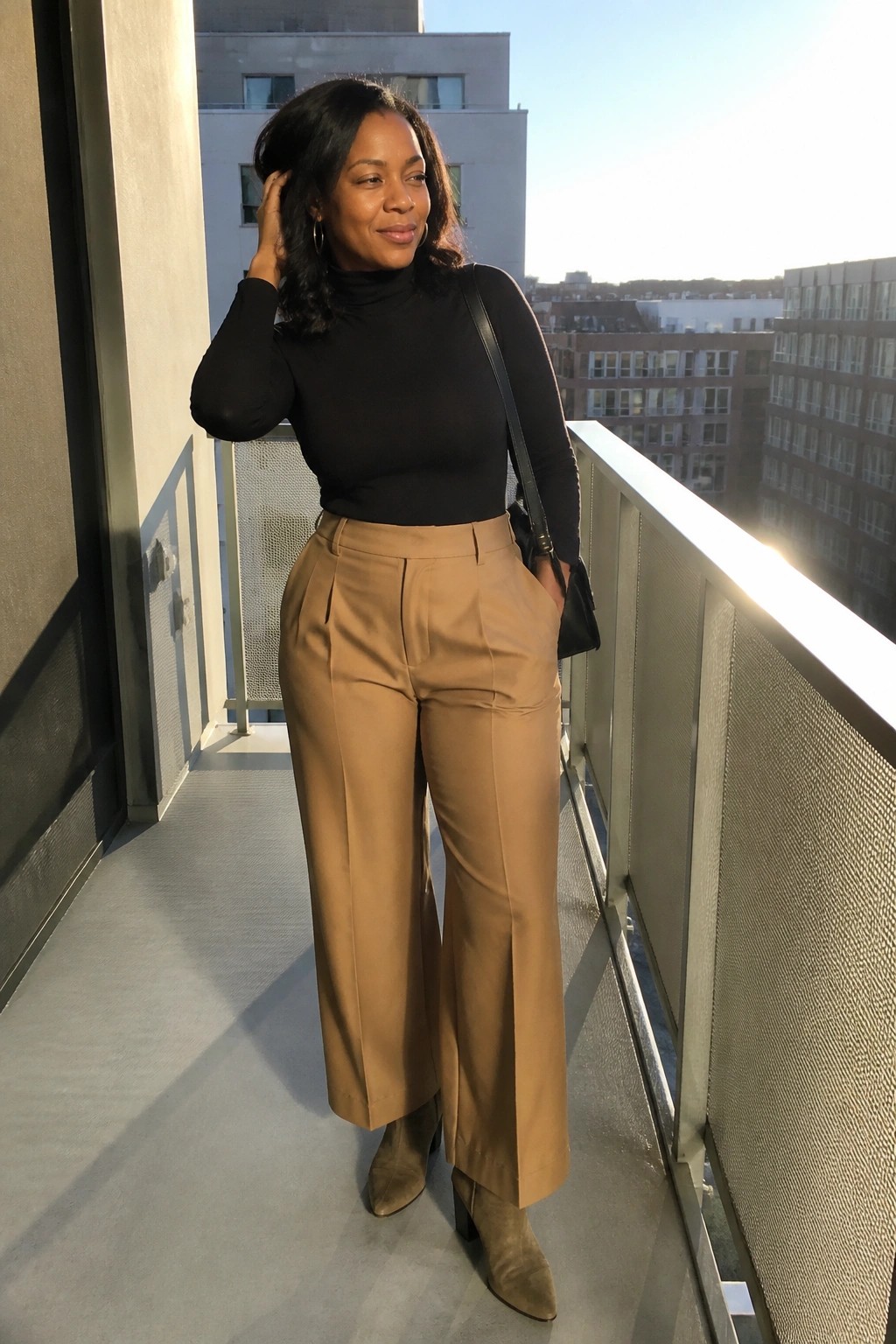 Woman in black turtleneck and tan wide-leg pants on sunny city balcony