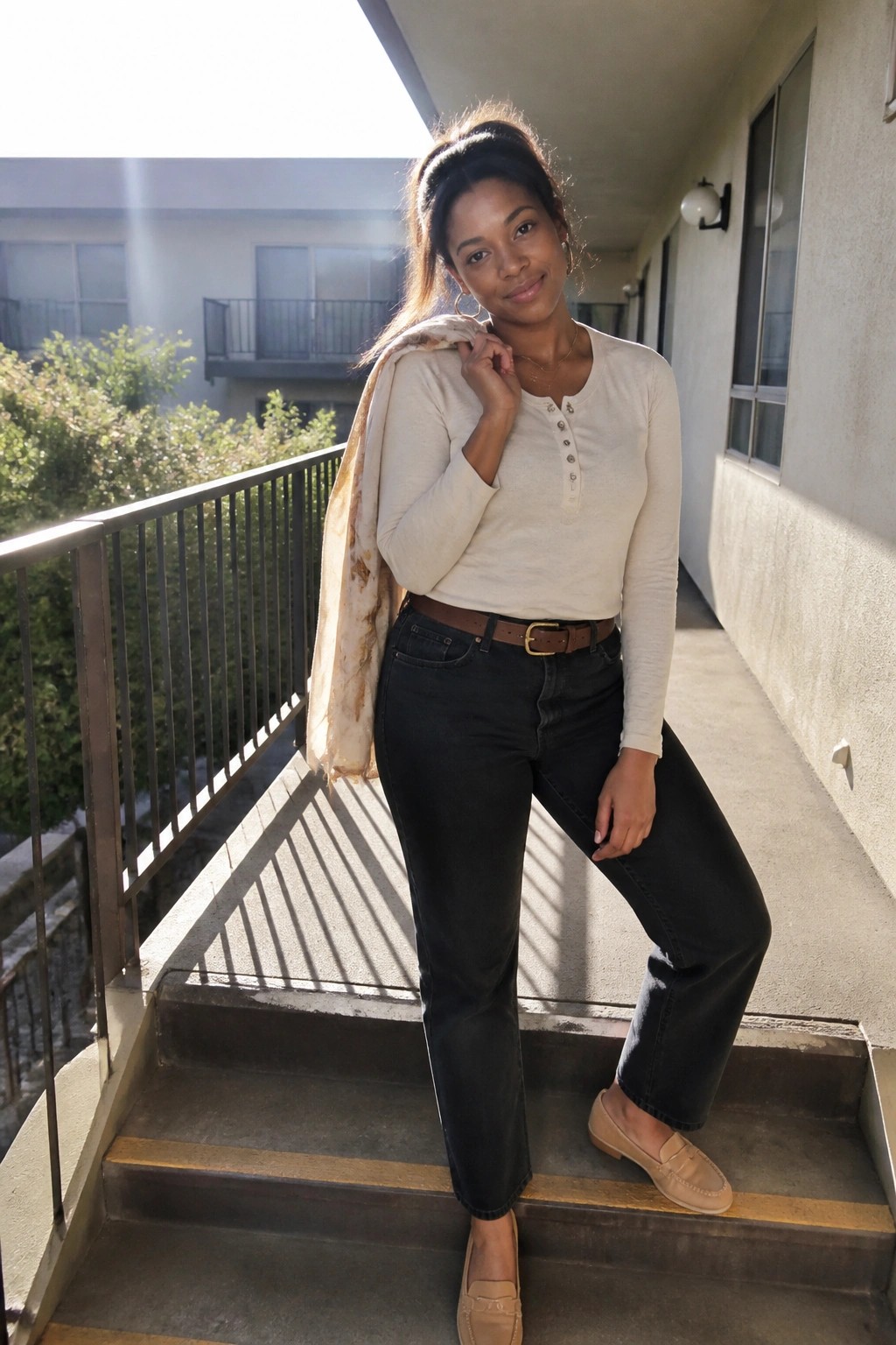 Woman in cream henley, dark jeans, and scarf posing on sunny outdoor stairs
