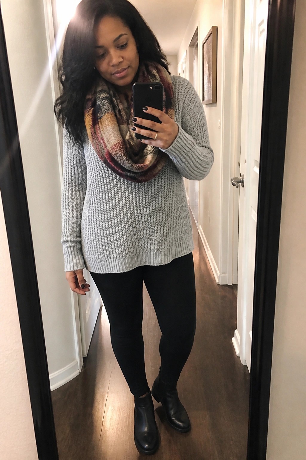 Woman in gray knit sweater and plaid scarf taking mirror selfie in hallway