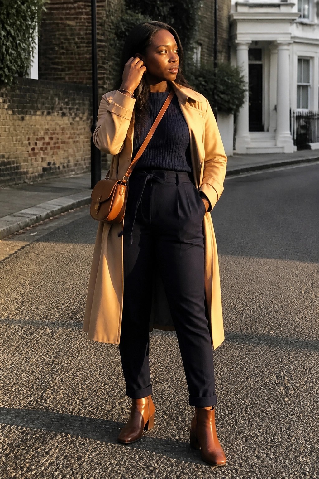 Woman in tan trench coat, navy sweater and pants, brown boots on city street