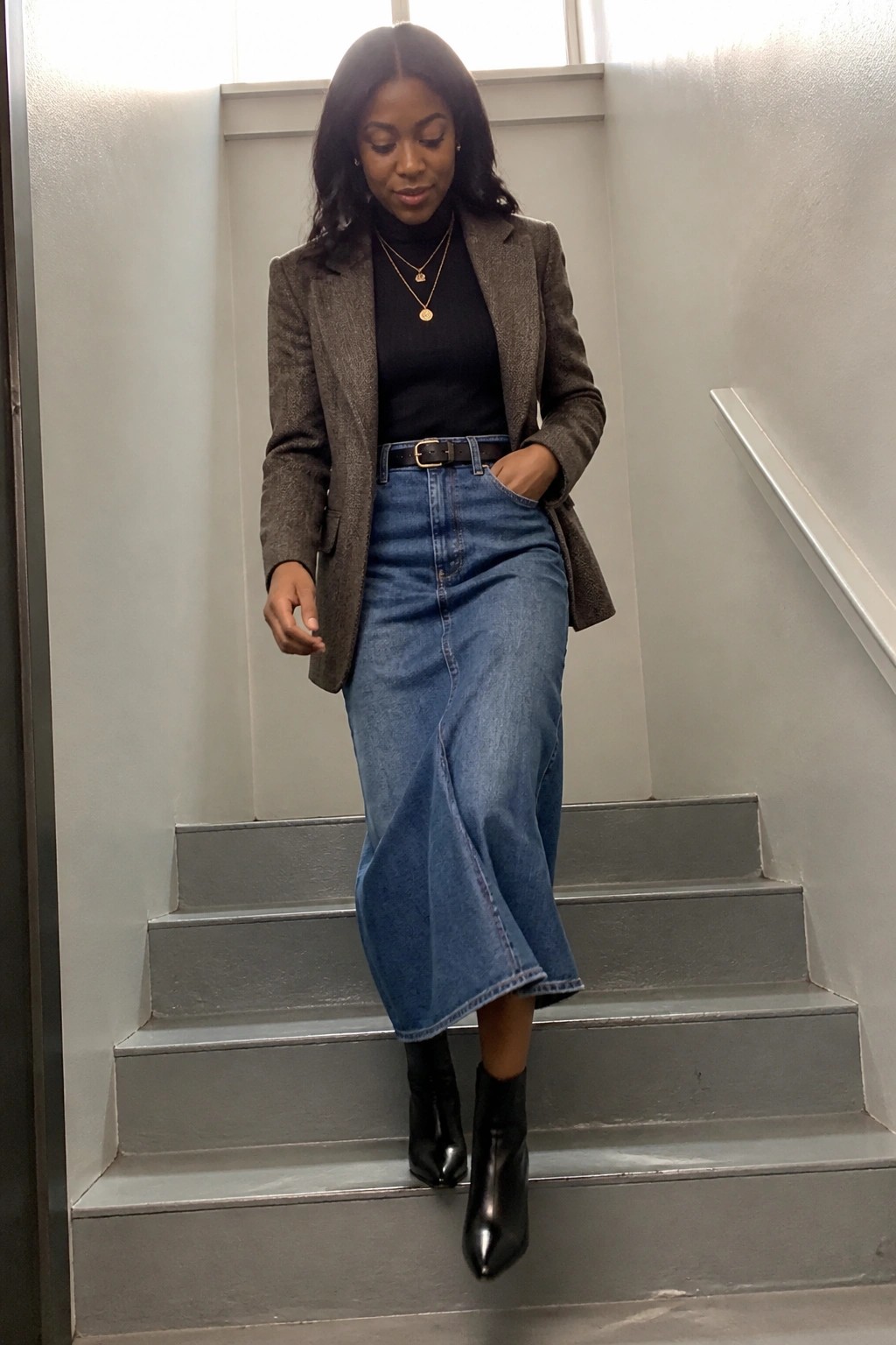 Woman in tweed blazer and midi denim skirt on gray stairs