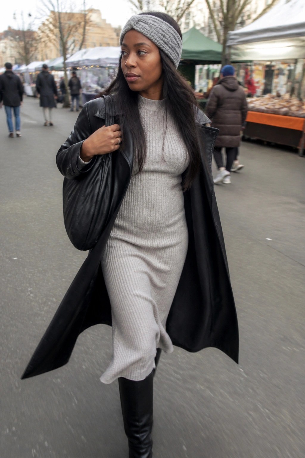 Woman in gray ribbed midi dress layered under open black leather coat, paired with black knee-high boots, matching gray knit headband, and black leather bag.