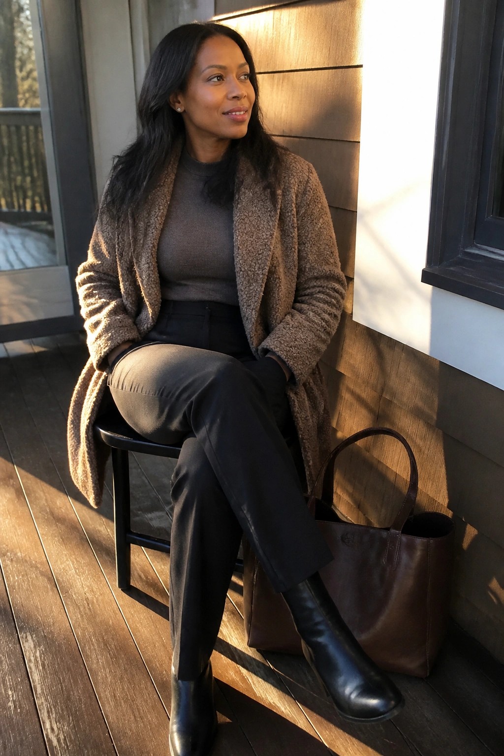 Woman in brown teddy coat and black boots on porch beside leather bag