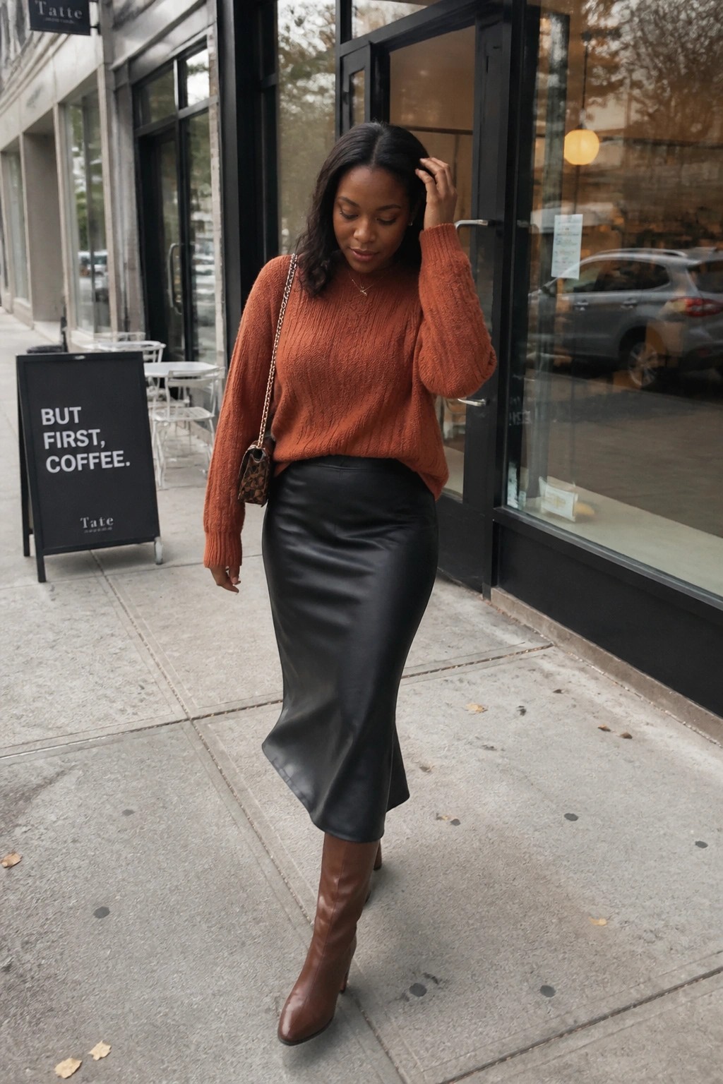 Woman in orange knit sweater and black leather skirt on city sidewalk
