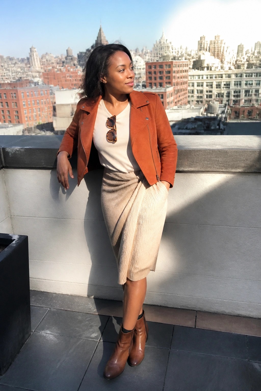 Woman in rust suede jacket and beige skirt on sunny city rooftop