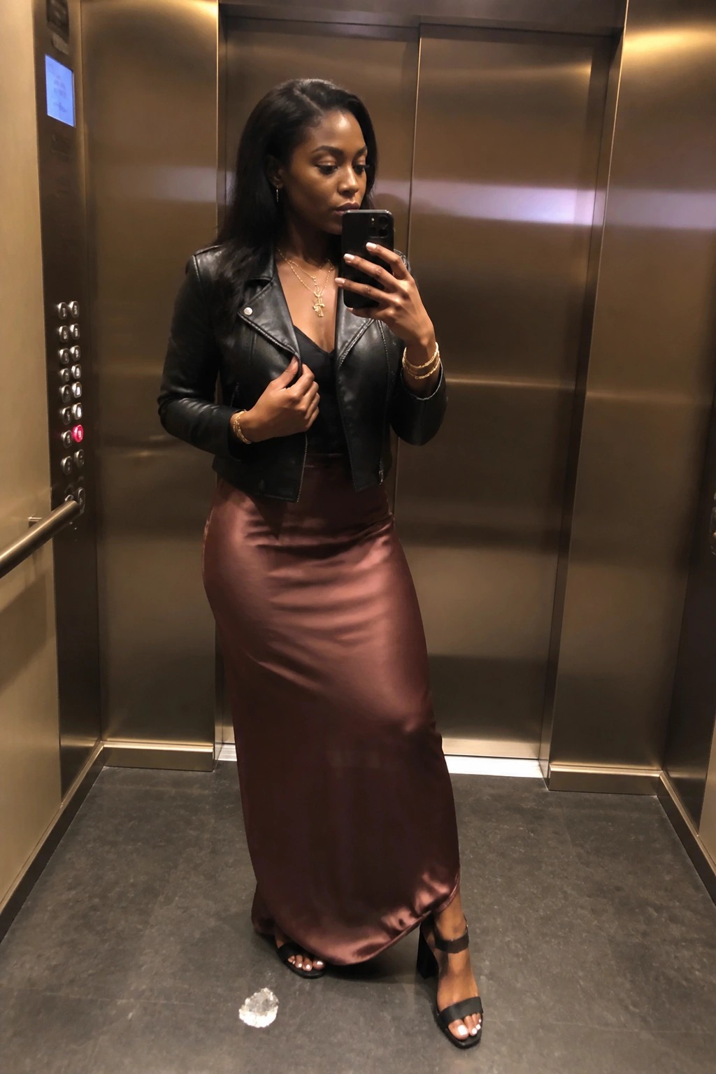 Woman in black leather jacket and brown satin skirt taking elevator selfie