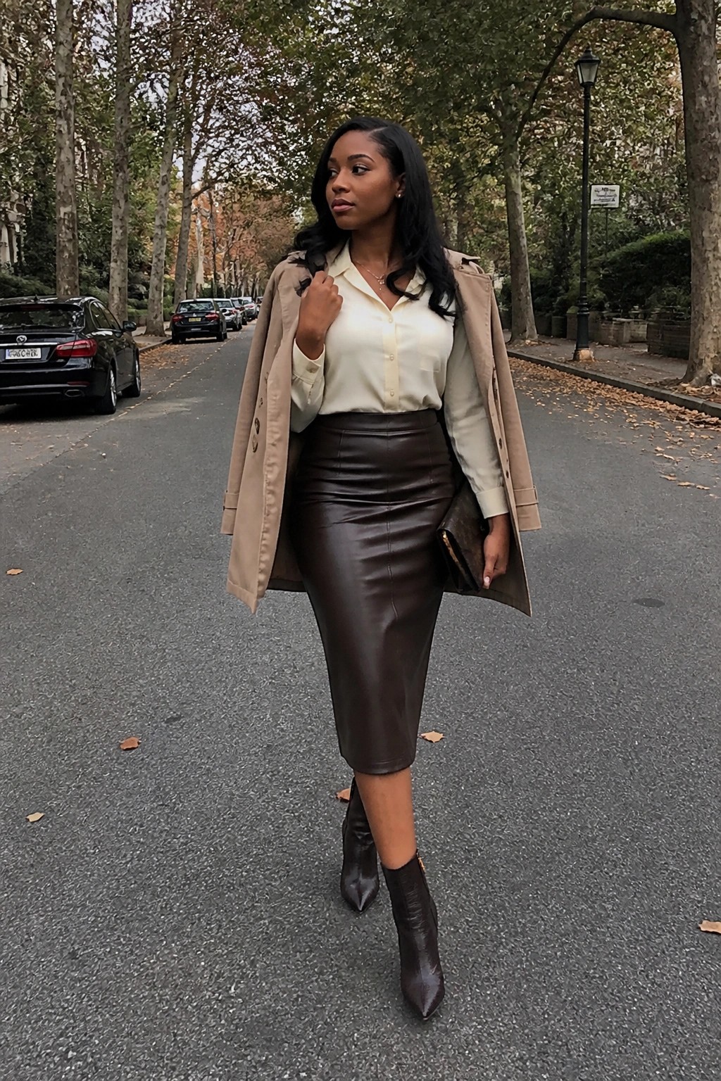 Woman in beige trench coat, cream blouse and brown leather skirt on autumn street