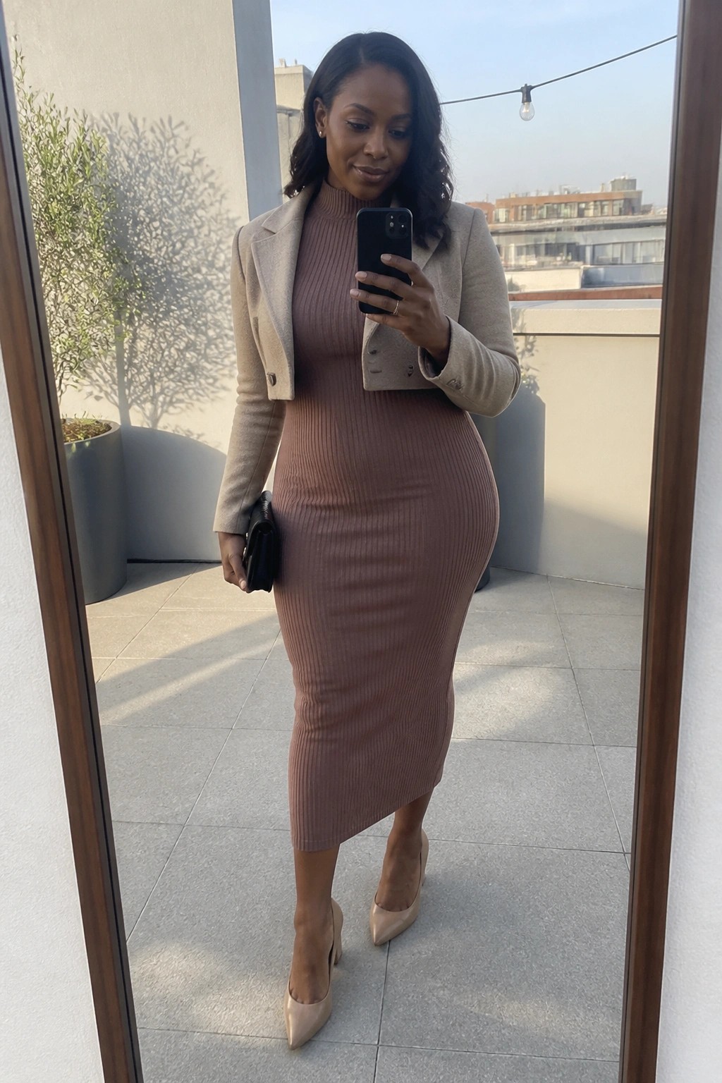 Woman in dusty rose ribbed dress and beige cropped blazer taking balcony mirror selfie