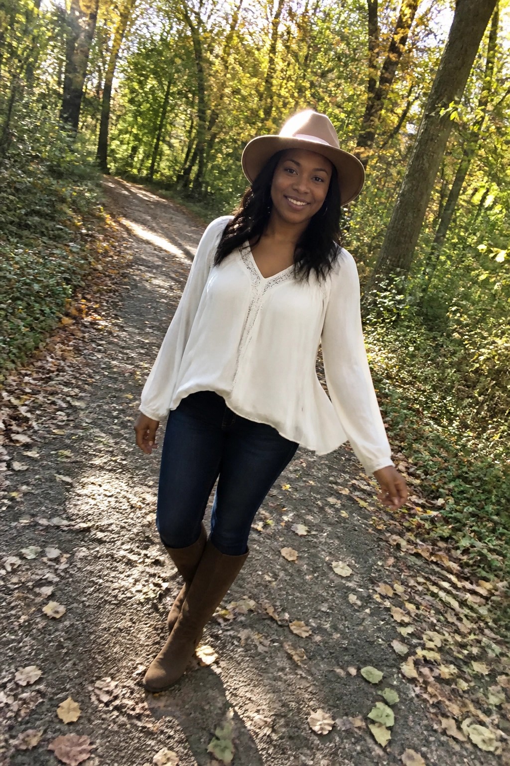 Woman in white blouse and hat on sunlit autumn forest path