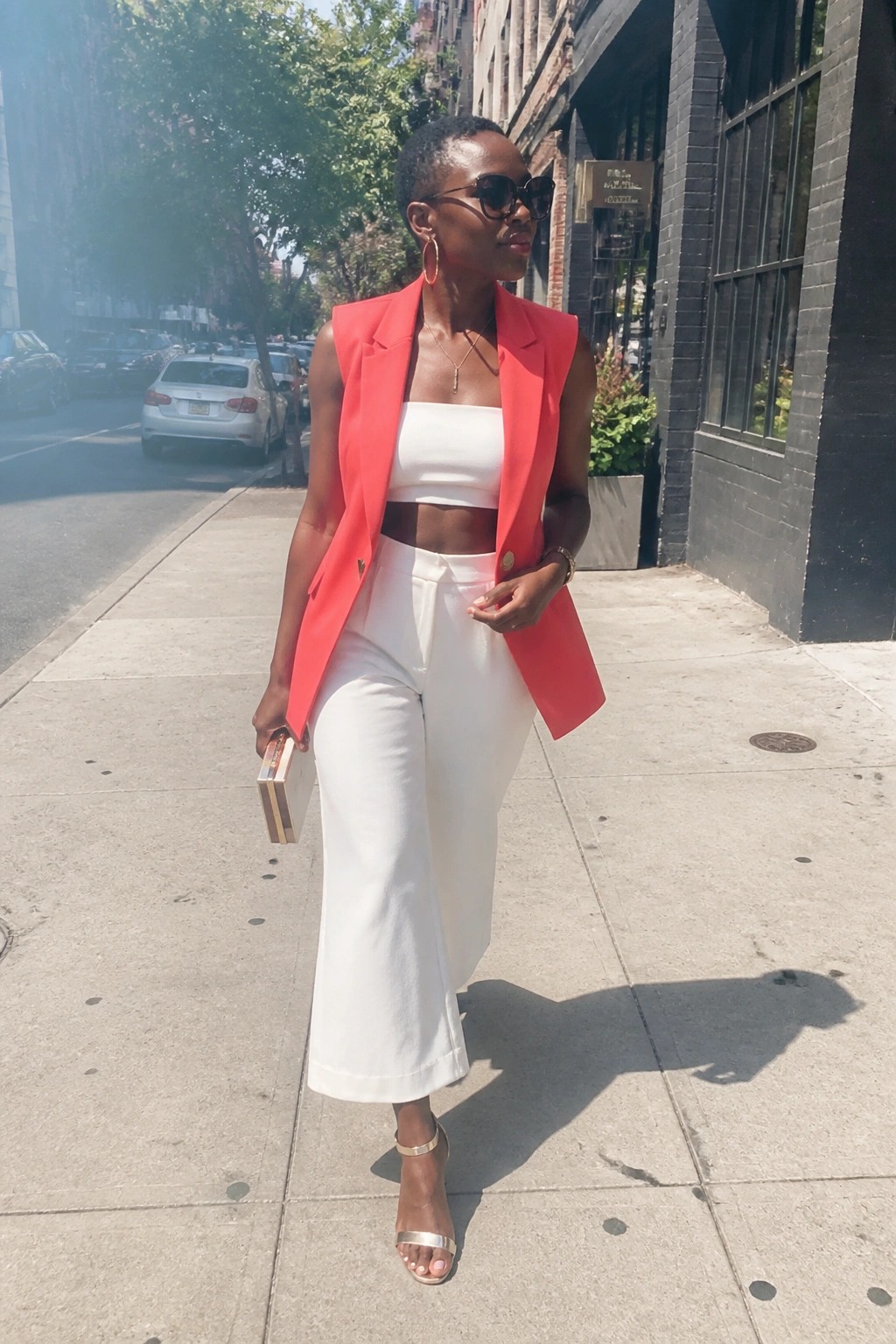 Woman in coral sleeveless blazer and white wide-leg pants on city sidewalk