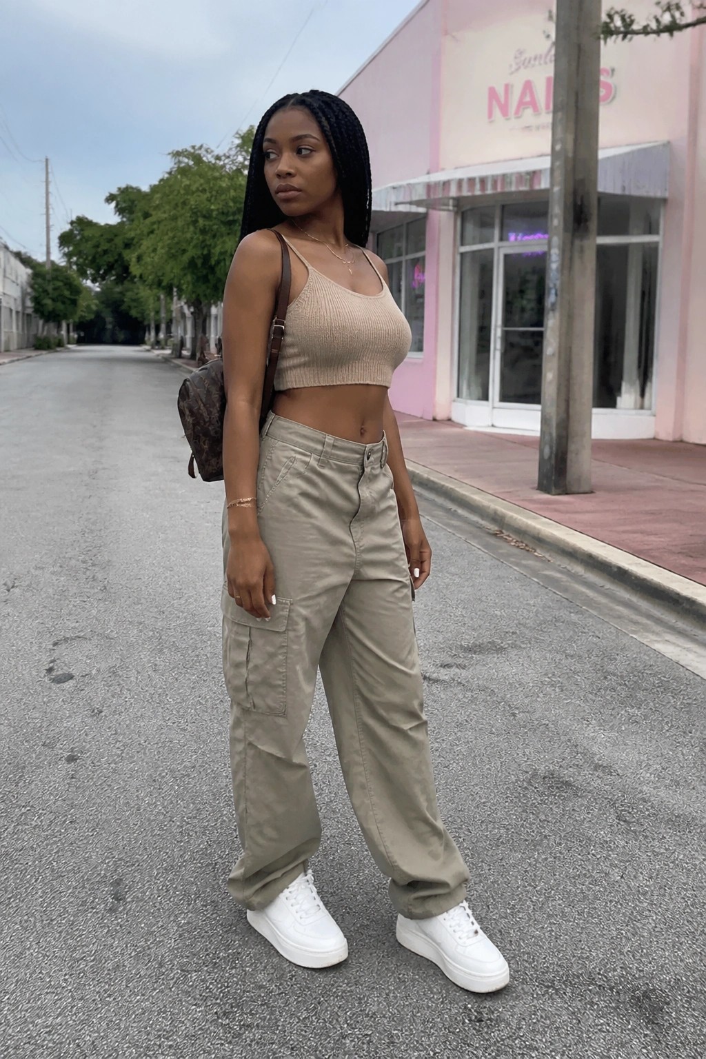 Woman with long braids in beige crop top and cargo pants with backpack outdoors