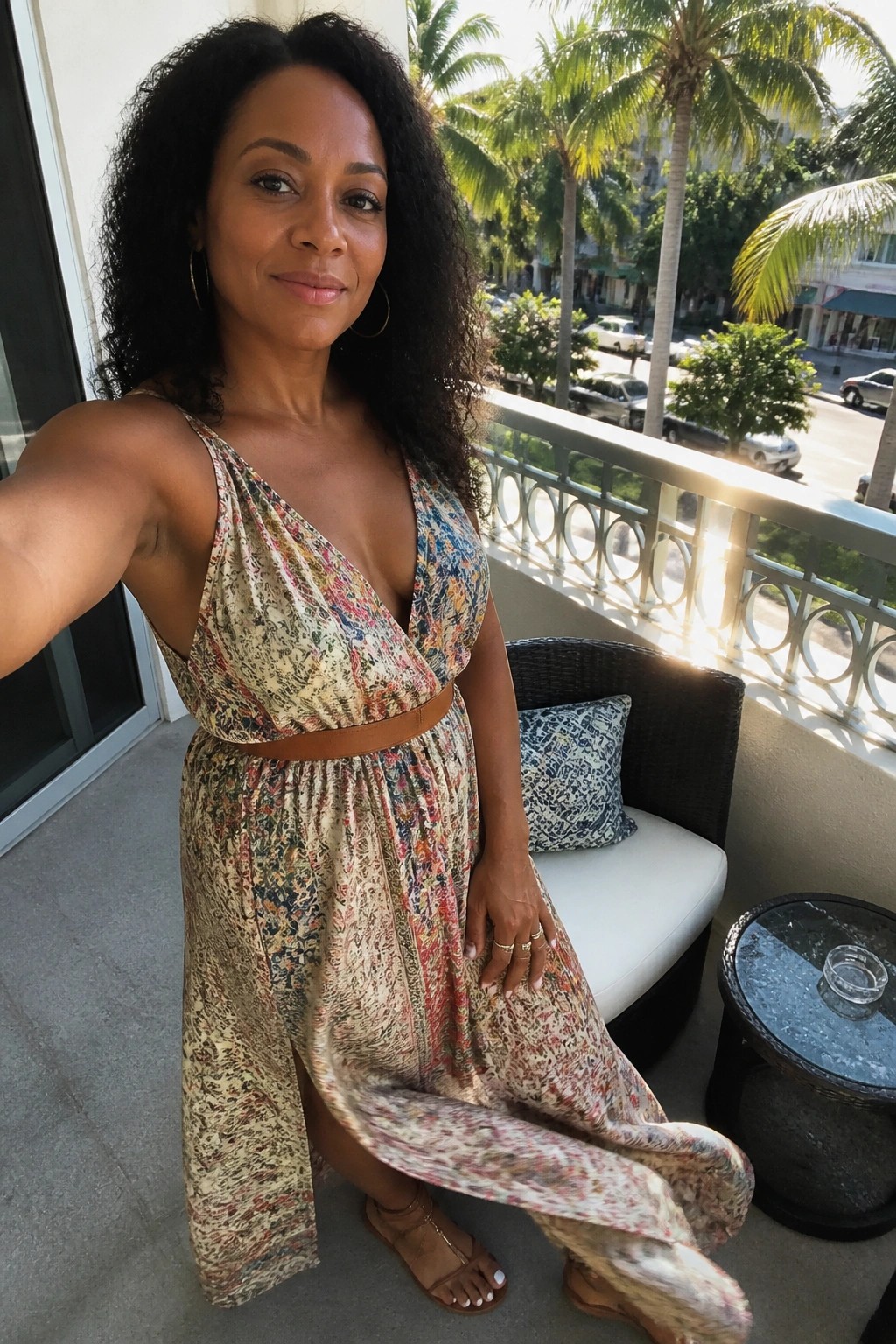 Woman in floral sundress posing on sunny balcony with palm trees nearby