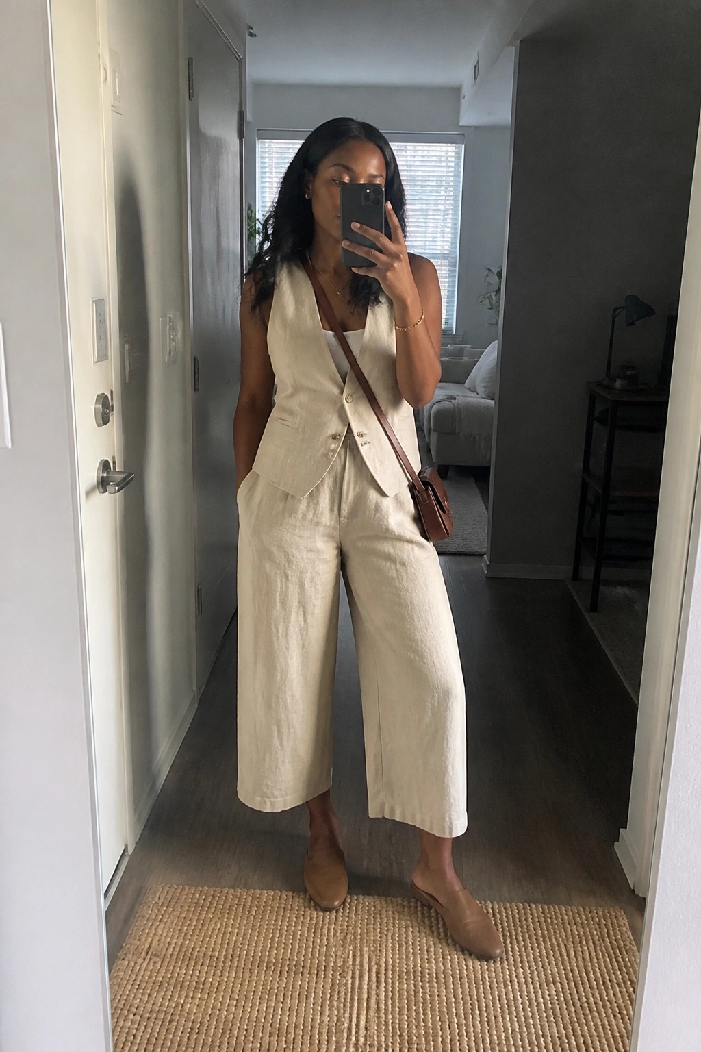 Woman in cream linen vest and wide pants taking mirror selfie in hallway