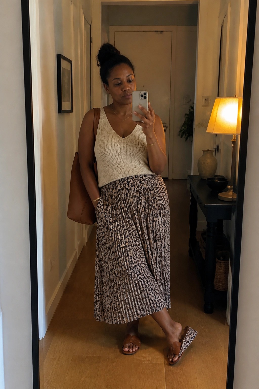 Woman in cream knit top and pleated animal-print skirt taking mirror selfie in hallway