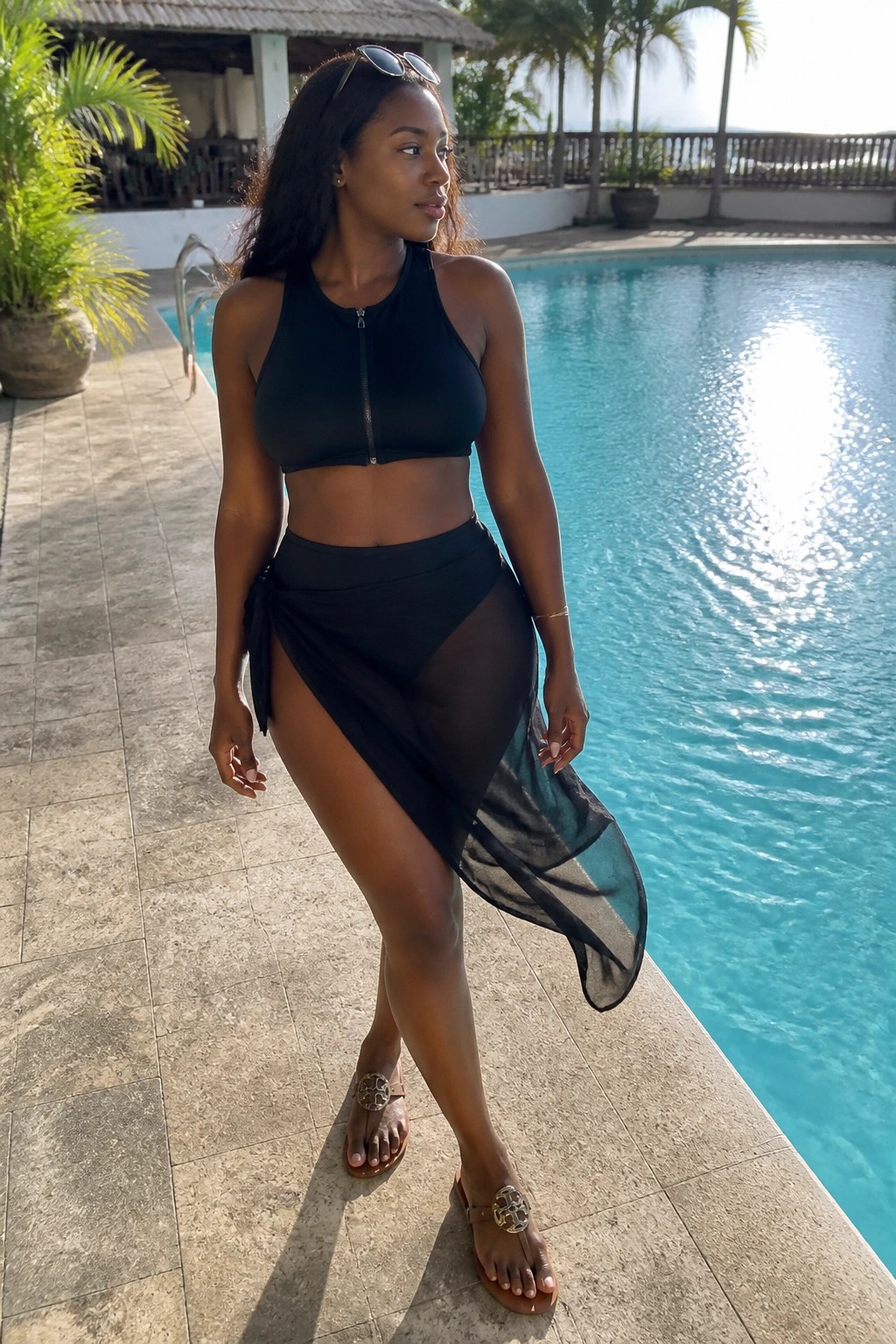 Woman in black crop top and sheer sarong standing by sunny pool