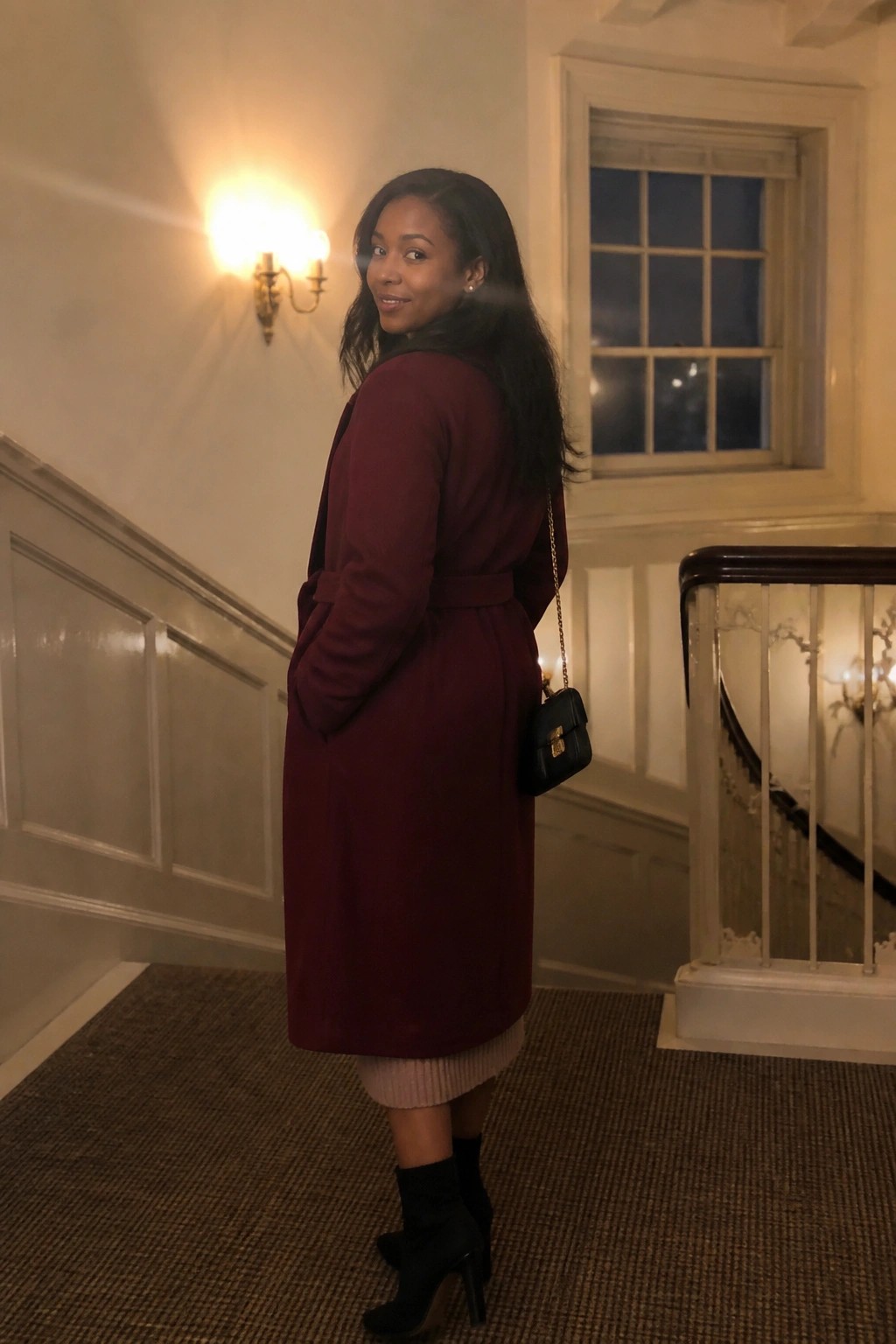 Woman in maroon coat looking back on elegant indoor staircase at night