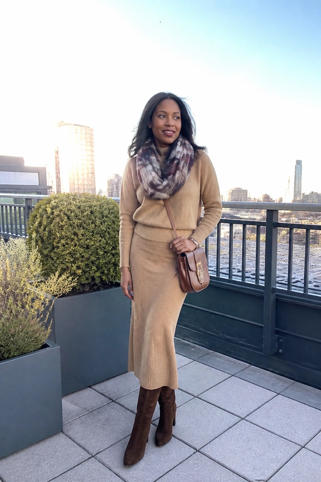 Woman in tan knit sweater and skirt with plaid scarf on sunny city rooftop