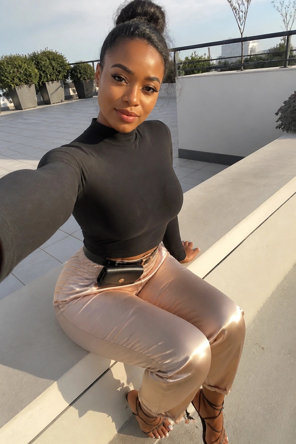 Woman in black crop top and shiny pink pants taking rooftop selfie