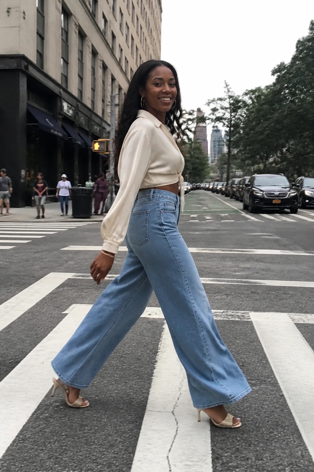 Woman in cream crop top and blue wide-leg jeans crossing city crosswalk
