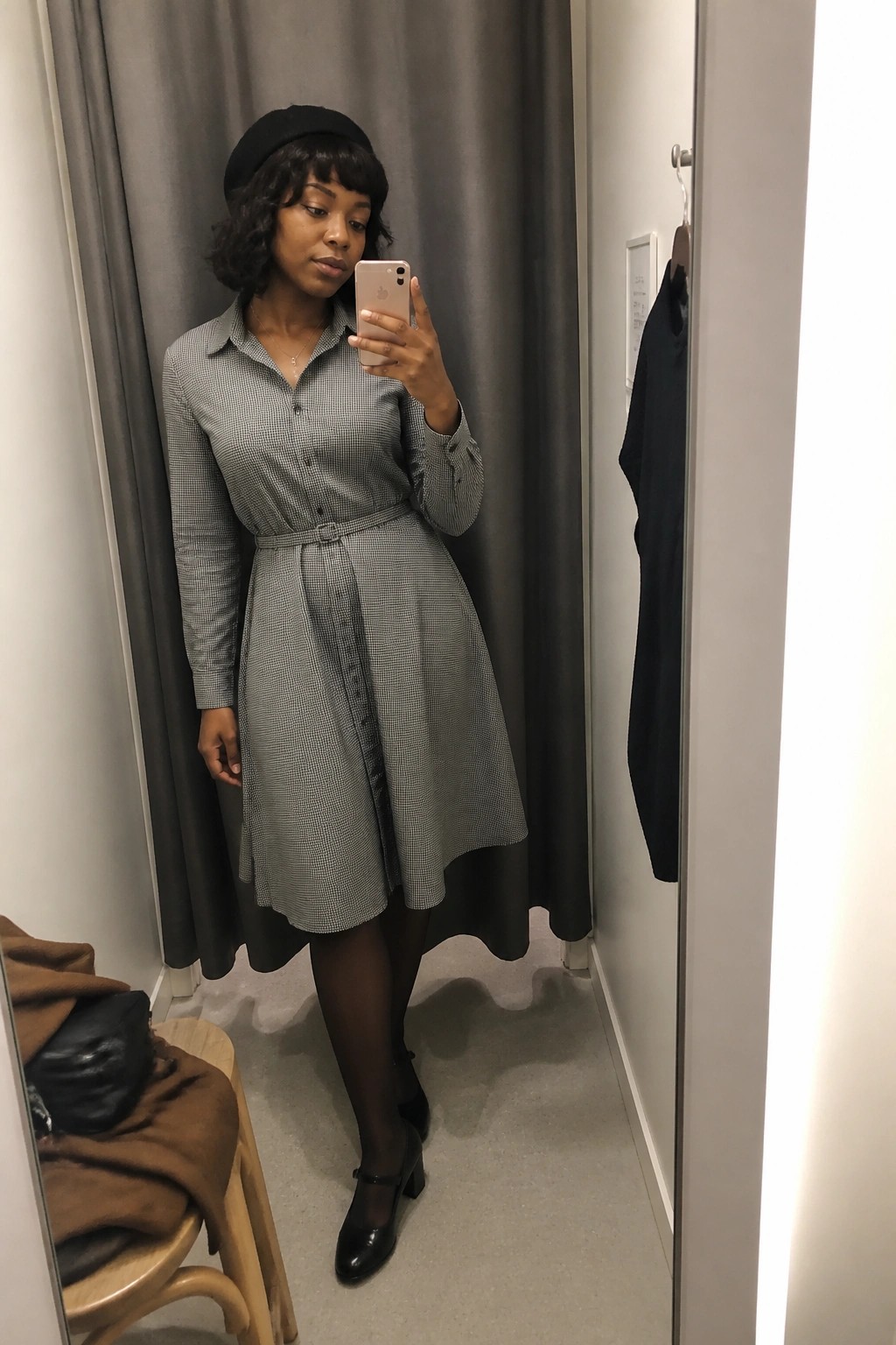 Woman in checkered dress and black beret taking mirror selfie in fitting room