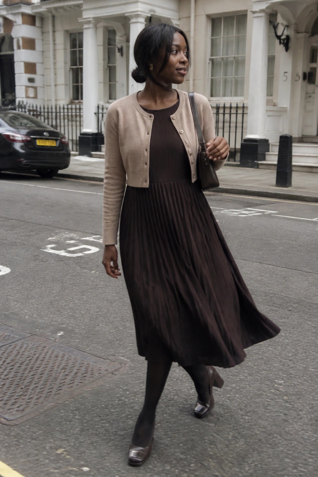 Woman in beige cardigan and brown pleated dress walking on city street